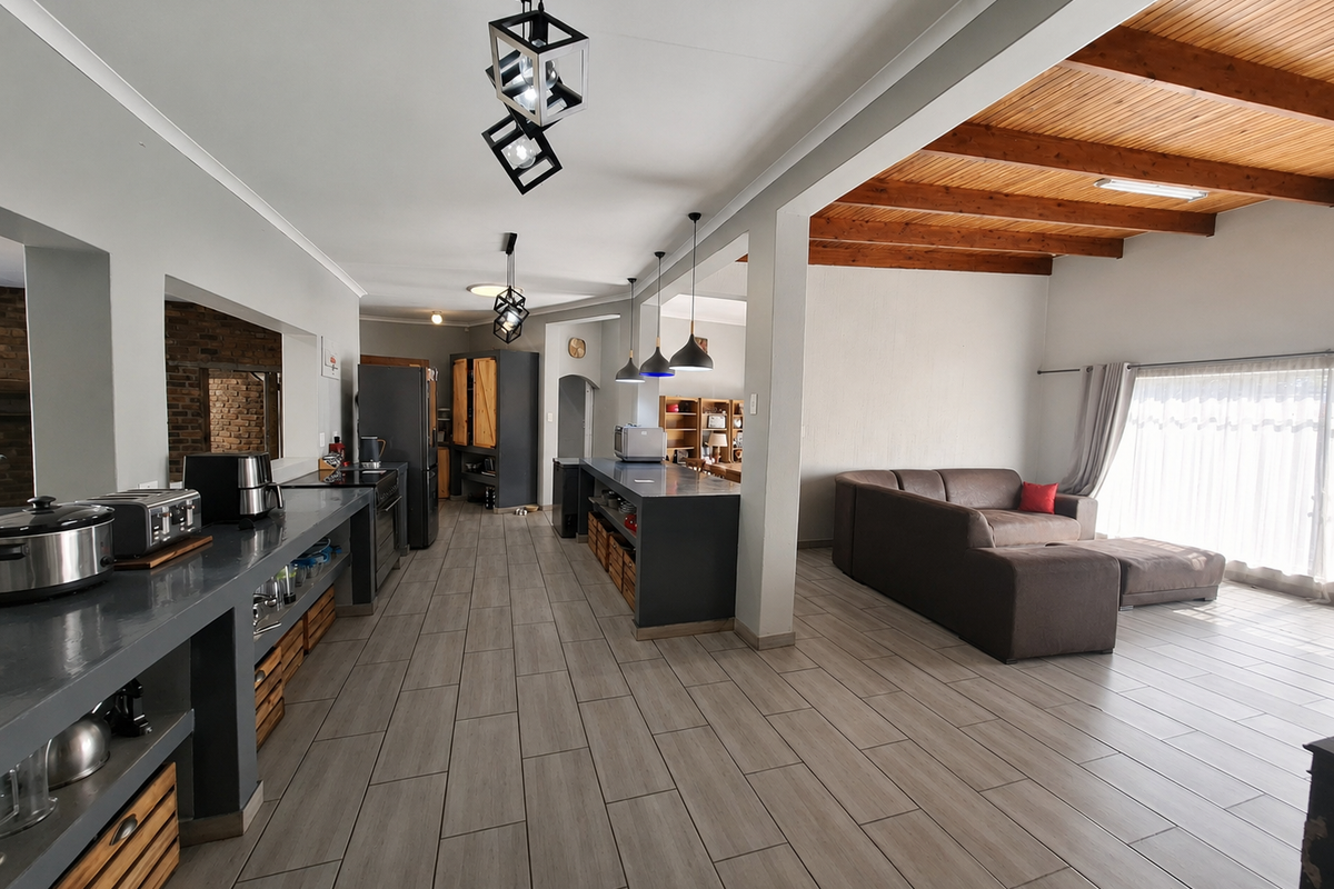 Spacious open-plan living and kitchen area featuring modern tiled floors, exposed timber ceiling beams, and a functional kitchen island with integrated cabinetry.