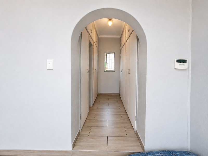 A clean, well-maintained hallway featuring an arched entrance, extensive built-in storage cupboards, and neutral tiled flooring.