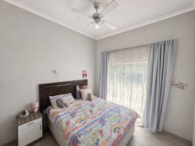 A well-maintained bedroom featuring laminate flooring, a ceiling fan, and large windows dressed with curtains.