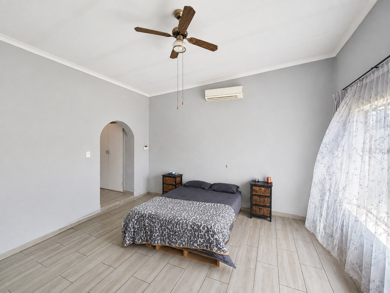 Spacious bedroom featuring light-toned tiled flooring, a ceiling fan, split-system air conditioning, and an arched entryway leading to a built-in cupboard area.