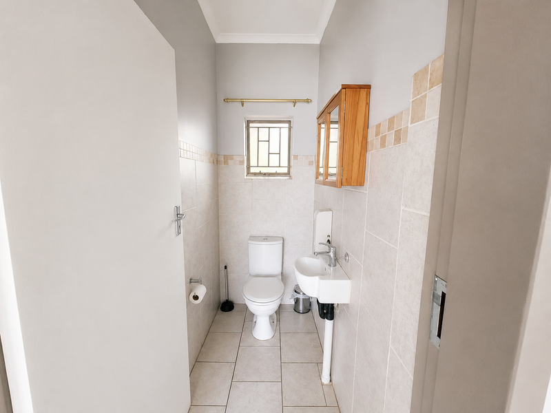 A compact, well-maintained guest bathroom featuring neutral wall and floor tiles, a wall-mounted basin, and a standard toilet.