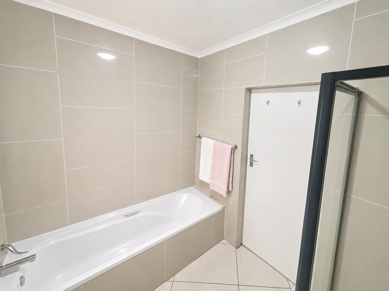 A modern, neutral-toned bathroom featuring a built-in bathtub, tiled walls and flooring, and a separate shower enclosure.