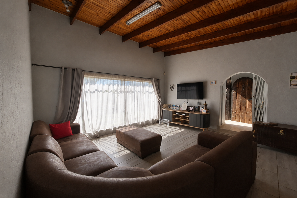 Spacious living room featuring a high exposed timber beam ceiling, tiled flooring, and an arched doorway leading to the entrance.