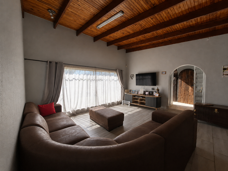 Spacious living room featuring a high exposed timber beam ceiling, tiled flooring, and an arched doorway leading to the entrance.