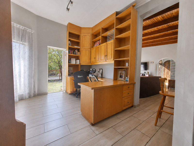 A functional home office space featuring extensive built-in wooden cabinetry and desk, tiled flooring, and direct access to the garden.