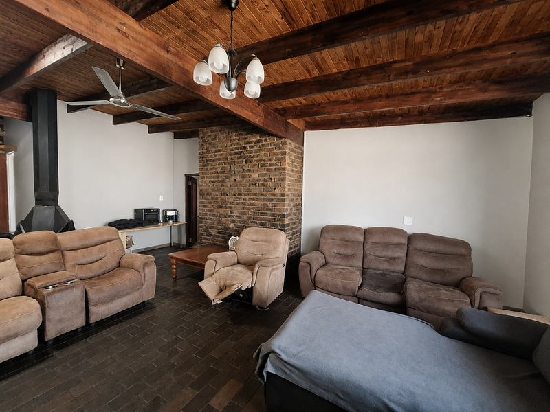 Spacious living room featuring a rustic exposed timber beam ceiling, a prominent brick fireplace, and durable tiled flooring.