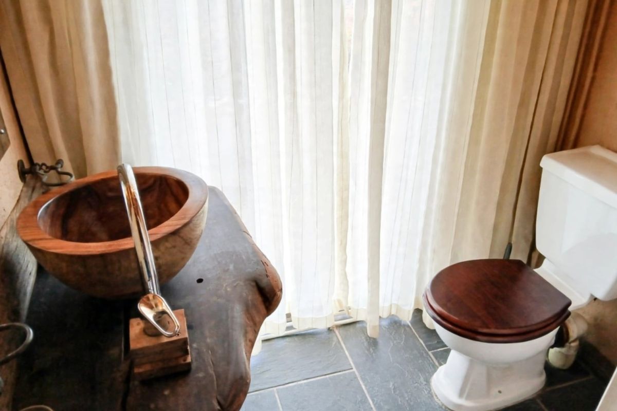 A rustic bathroom featuring a unique live edge wood vanity with a vessel sink, chrome faucet, and slate floor tiles.
