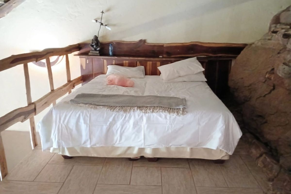 A rustic bedroom featuring a unique natural rock wall, tiled flooring, and a custom timber headboard with an integrated wooden railing.