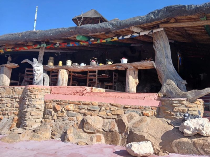 Rustic outdoor patio area featuring a traditional thatched roof, natural stone masonry, and integrated timber support structures.