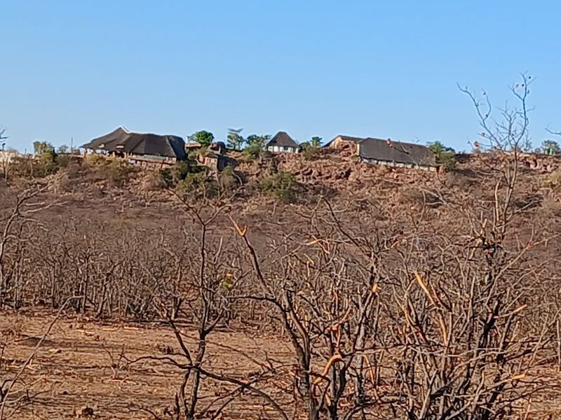 A distant view of a farm property featuring multiple structures with traditional thatched roofs situated on a rocky hillside.