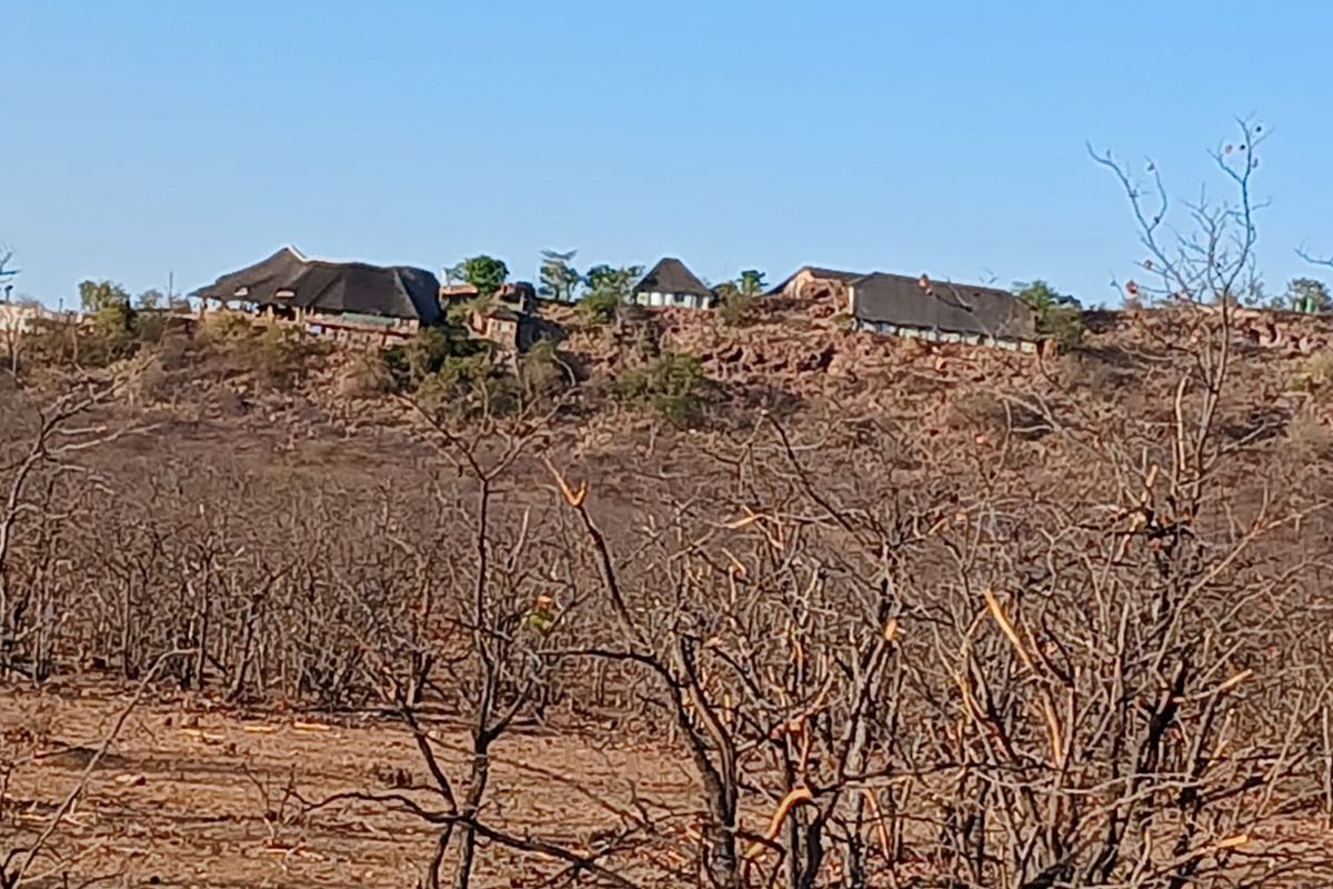 A distant view of a farm property featuring multiple structures with traditional thatched roofs situated on a rocky hillside.