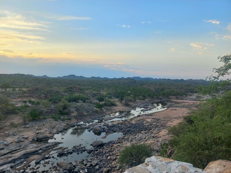 A scenic landscape view overlooking a rocky riverbed and natural bushveld terrain, showcasing the expansive rural surroundings of the property.