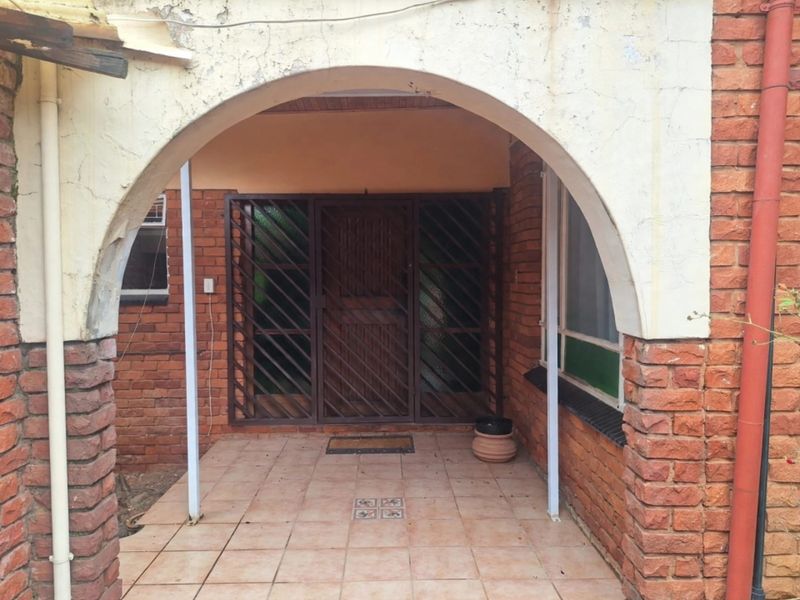 Covered entrance porch featuring an arched masonry design, exposed brick walls, and a secure metal gate at the main doorway.