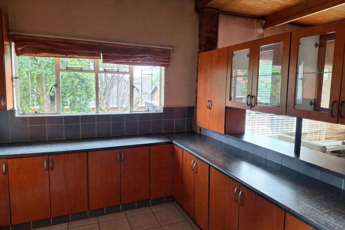 A functional kitchen featuring timber cabinetry, dark laminate countertops, tiled backsplash, and a distinctive timber ceiling, offering a classic layout with ample storage space.