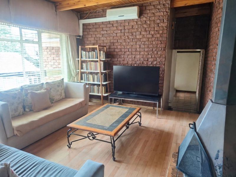 Cozy living room featuring an exposed brick feature wall, timber ceiling beams, laminate flooring, and a built-in fireplace for added warmth.