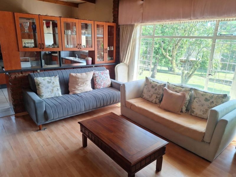 Open-plan living area featuring exposed brickwork, timber ceiling beams, and built-in cabinetry, with large windows providing natural light and garden views.