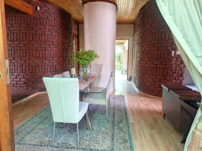 Dining area featuring distinctive curved exposed brick walls, timber ceiling, and laminate flooring, creating a unique architectural space with direct access to the garden.