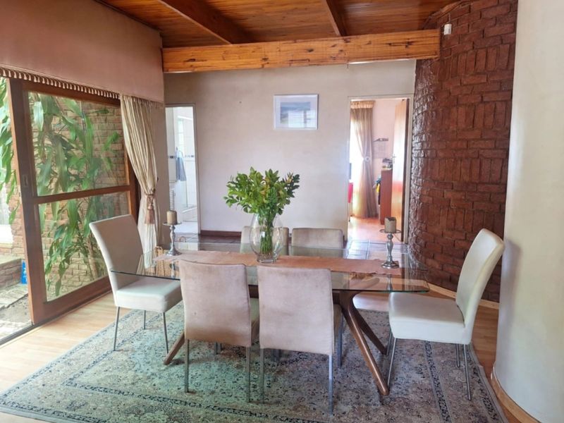 Dining room featuring exposed timber ceiling beams, a rustic brick feature wall, and large sliding glass doors providing natural light and garden access.