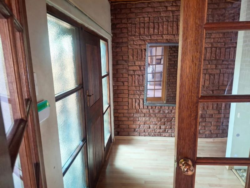 A bright hallway featuring exposed brickwork, laminate flooring, and timber-framed glass doors, creating a warm and textured transition space.