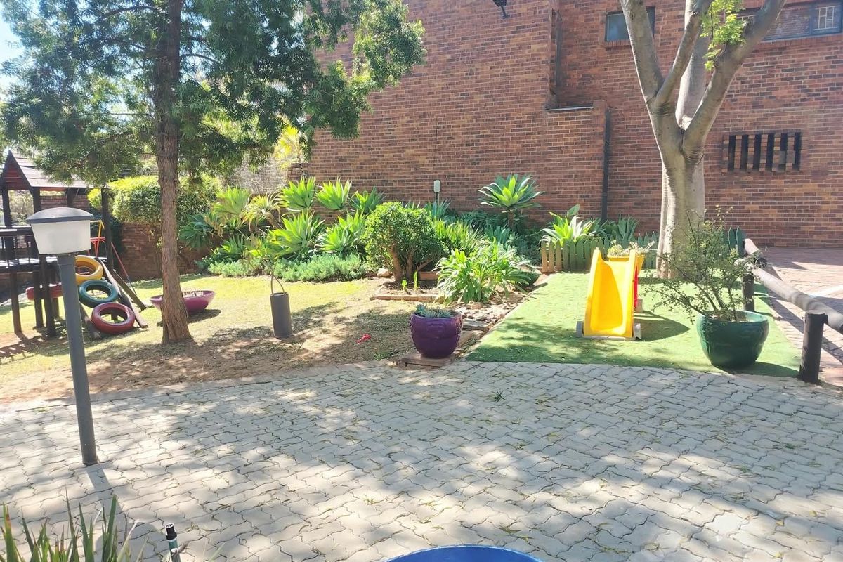 A rear garden area featuring a paved patio, artificial lawn, mature landscaping, and a brick townhouse facade.