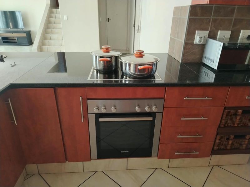 Kitchen area featuring dark granite countertops, built-in oven, electric hob, and wooden cabinetry with tiled flooring.
