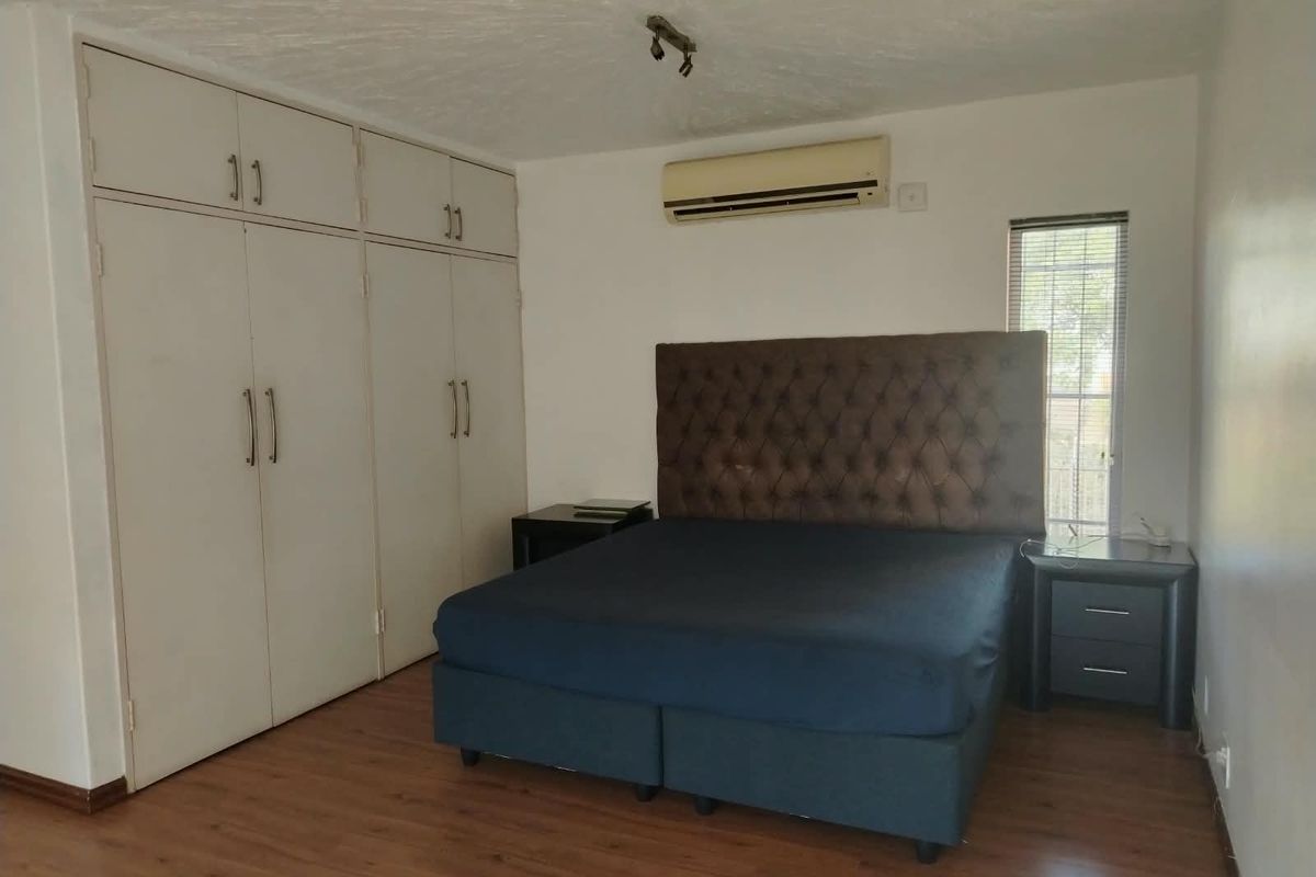 A bedroom featuring laminate flooring, built-in cupboards, and a wall-mounted split-system air conditioner.