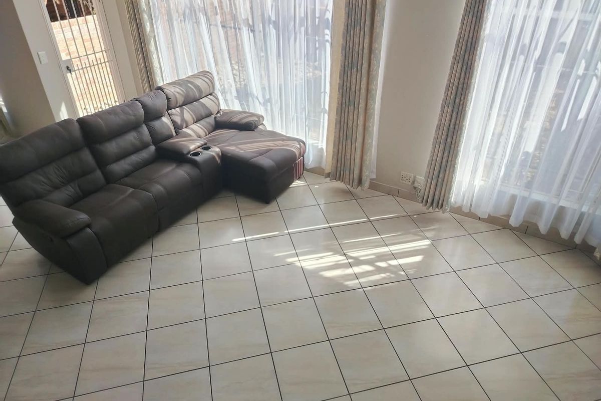 A bright living room featuring large sliding glass doors with curtain tracks and neutral tiled flooring throughout.