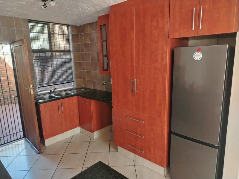 A functional kitchen featuring wood-finish cabinetry, dark countertops, a double basin sink, and tiled flooring with direct access to an outdoor area.