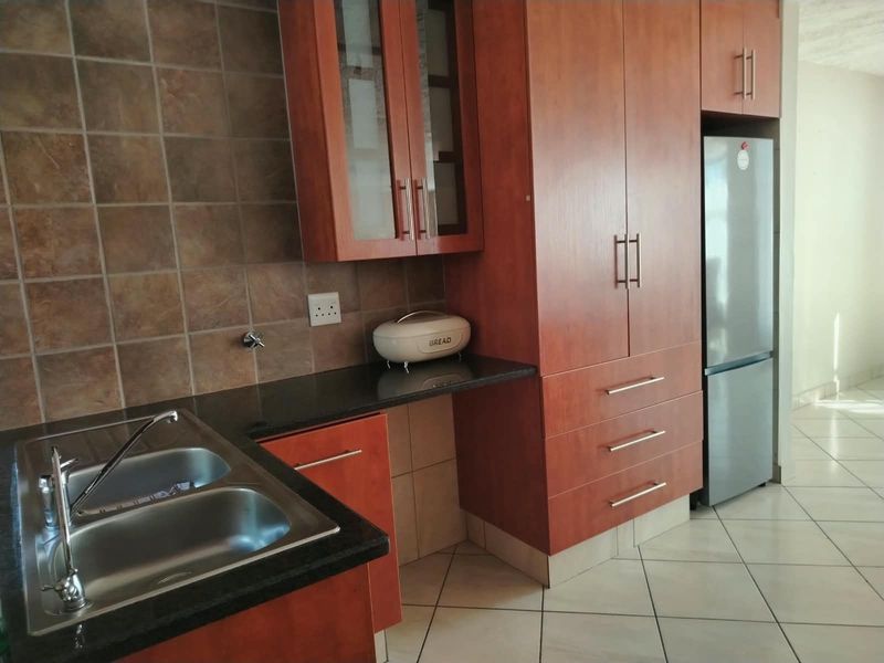 A functional kitchen featuring cherry-wood cabinetry, granite countertops, a double basin sink, and tiled flooring with a neutral backsplash.