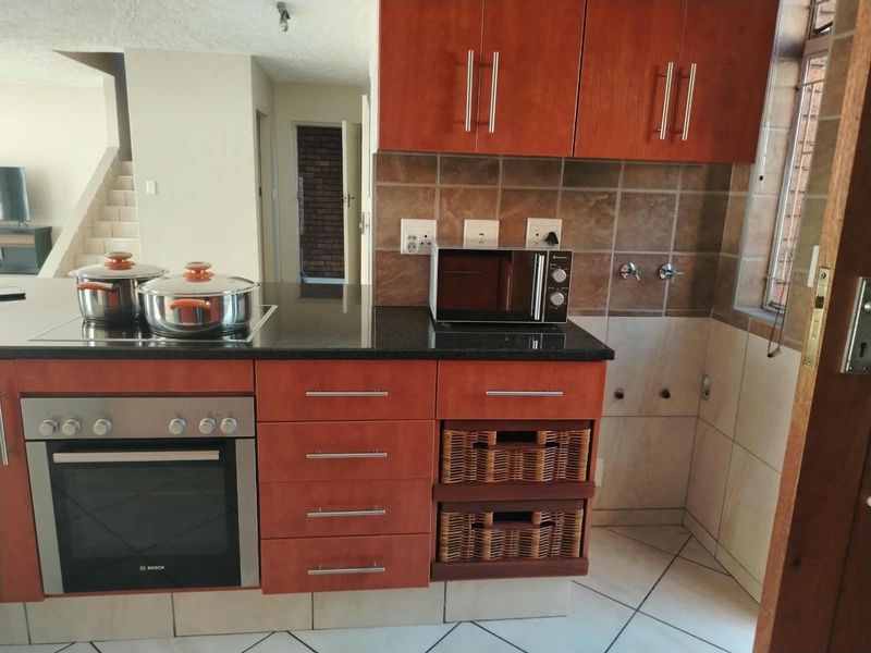 Kitchen area featuring wooden cabinetry, granite countertops, built-in oven, electric hob, and tiled finishes with dedicated plumbing connections for appliances.