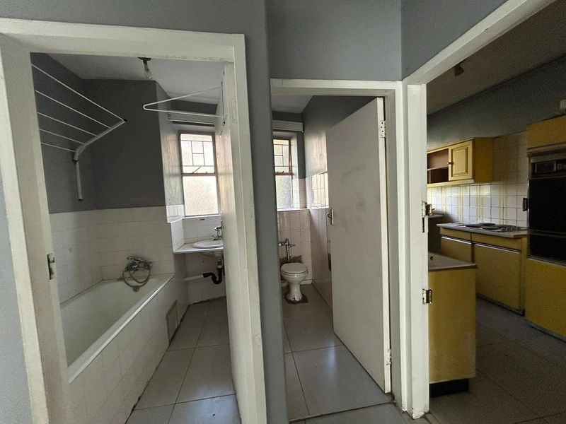 View of an apartment interior showing a bathroom, separate toilet, and dated kitchen area with built-in cabinetry and appliances.