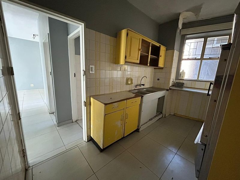 A dated kitchen featuring original cabinetry, a double basin sink, and tiled finishes, requiring renovation to modernize the space.