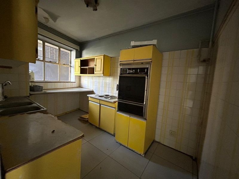 A dated kitchen featuring original yellow cabinetry, built-in oven, and tiled splashbacks, requiring significant renovation to modernize the space.