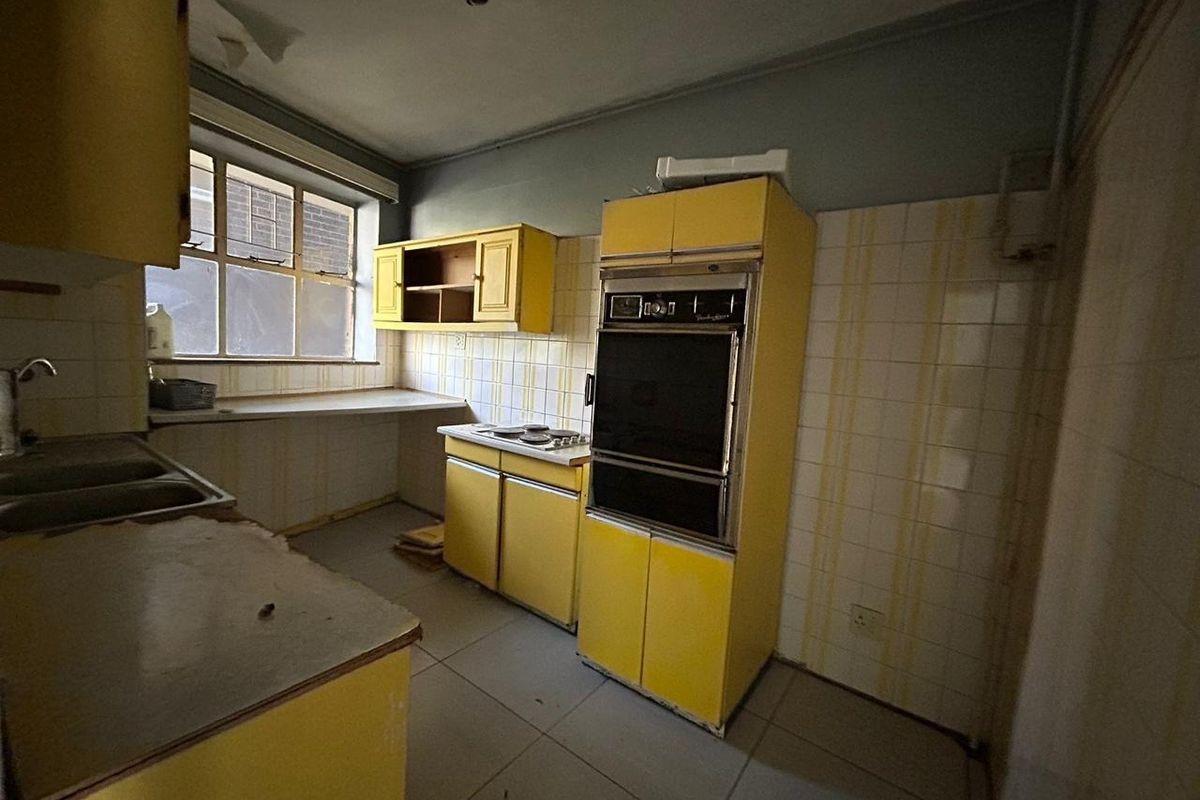 A dated kitchen featuring original yellow cabinetry, built-in oven, and tiled splashbacks, requiring significant renovation to modernize the space.