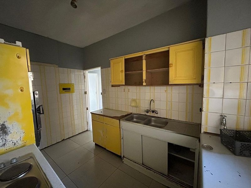 A dated kitchen featuring original yellow cabinetry, tiled backsplash, and a double bowl sink, requiring significant renovation to modernize the space.