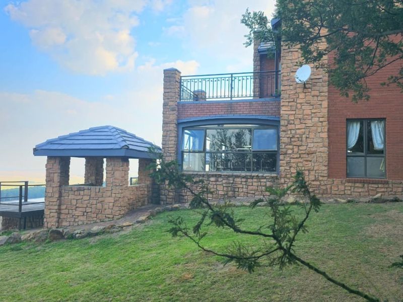 Rear view of the lodge featuring stone and brick exterior, a raised balcony with metal railings, and a stone gazebo overlooking the landscape.