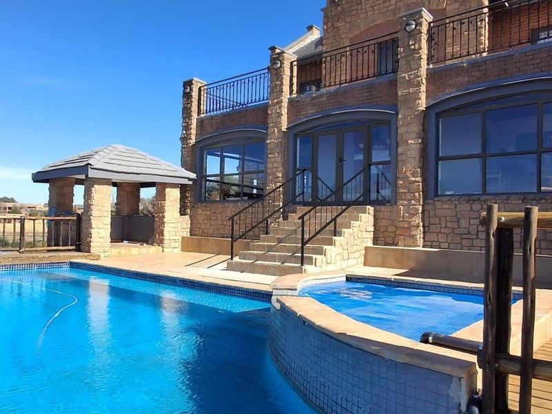 A well-maintained lodge exterior featuring a swimming pool, raised spa, stone-clad facade, and a covered gazebo area with access to an upper balcony.