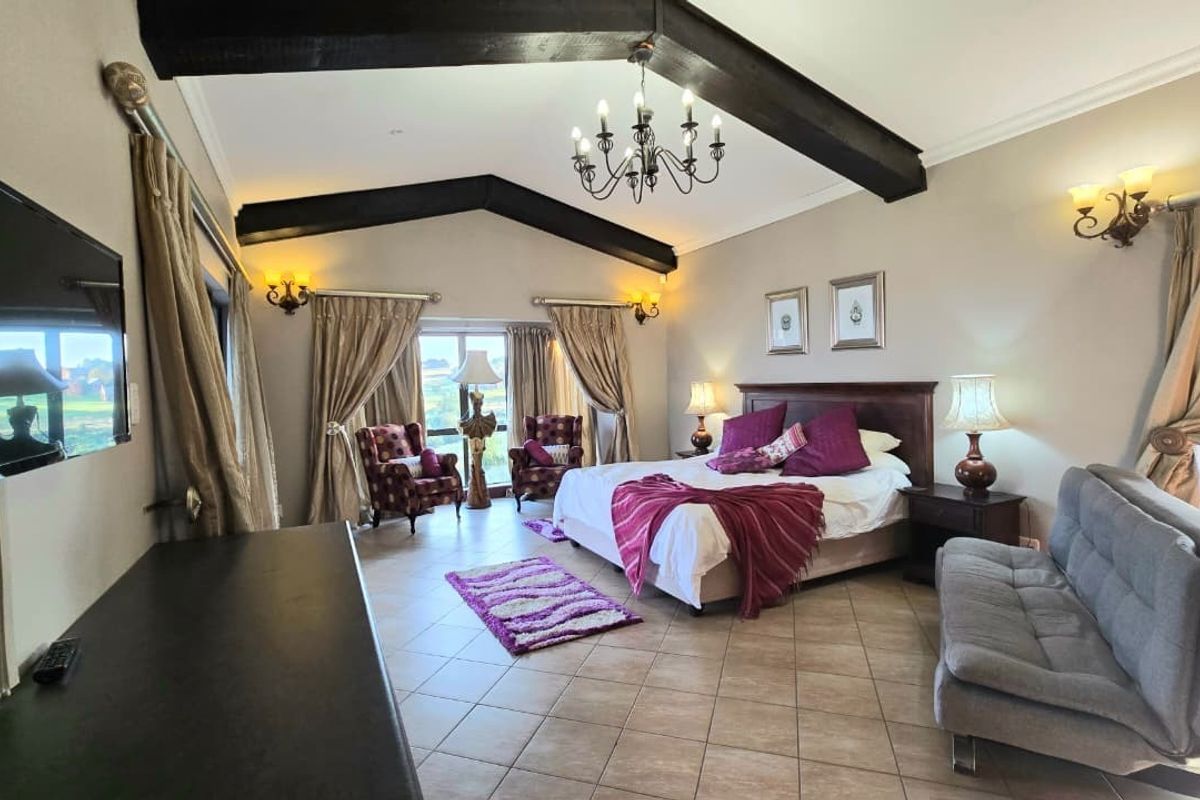 Spacious bedroom featuring vaulted ceilings with exposed timber beams, tiled flooring, and large windows providing natural light.