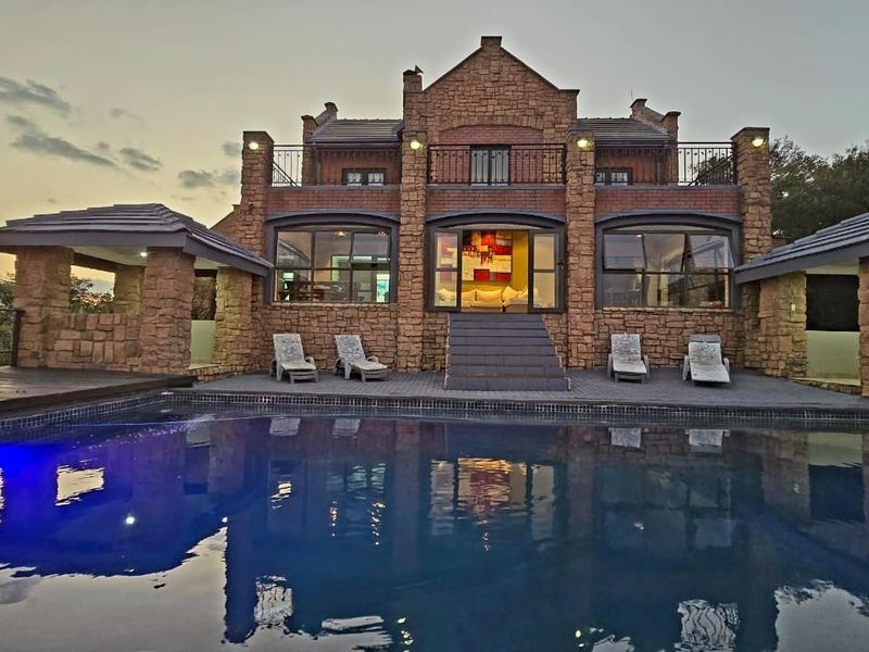 A stunning lodge exterior featuring a large swimming pool, stone-clad facade, and an elevated balcony overlooking the outdoor entertainment area.