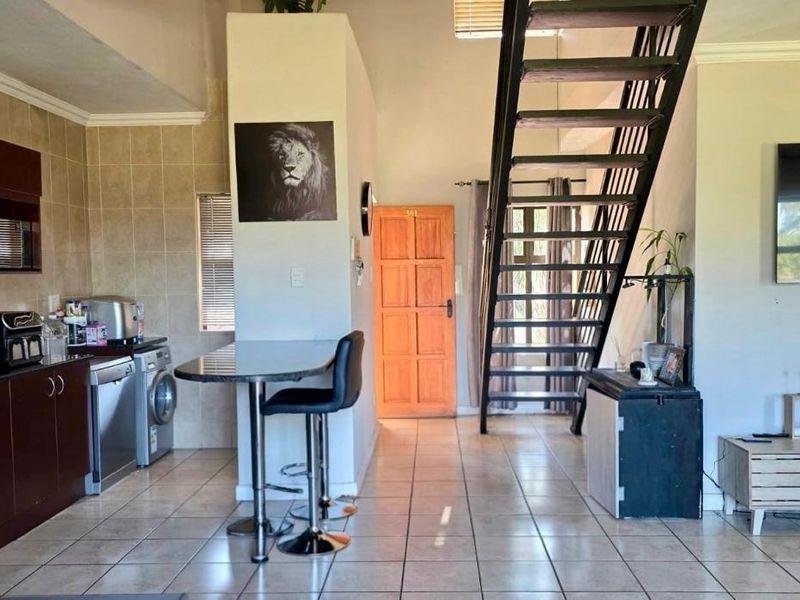Open-plan living area featuring a kitchen with granite countertops, tiled flooring, and a prominent metal staircase leading to the upper level.