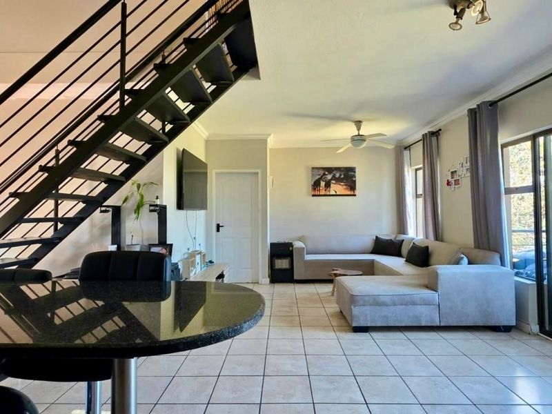 Spacious open-plan living area featuring tiled floors, a modern metal staircase, and large sliding glass doors providing access to the outdoor space.