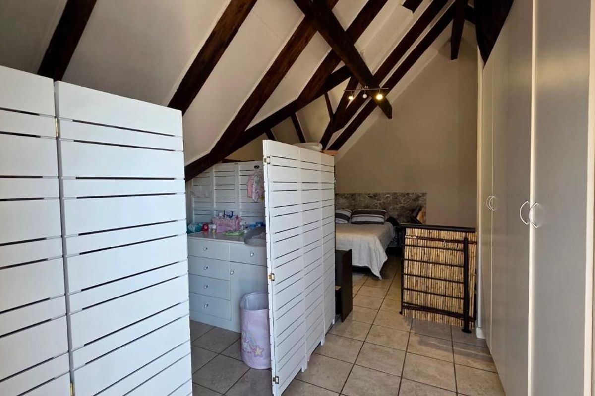 Attic-style bedroom featuring exposed timber rafters, vaulted ceilings, tiled flooring, and built-in storage cupboards.