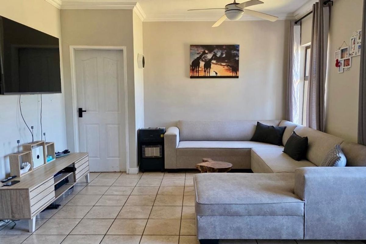 A comfortable living room featuring tiled flooring, coved cornicing, and a ceiling fan, providing a functional and well-lit space.