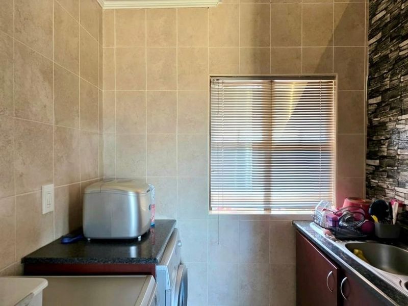 A functional laundry area featuring tiled walls, a stone-effect feature wall, built-in cabinetry, a stainless steel sink, and a window with venetian blinds.