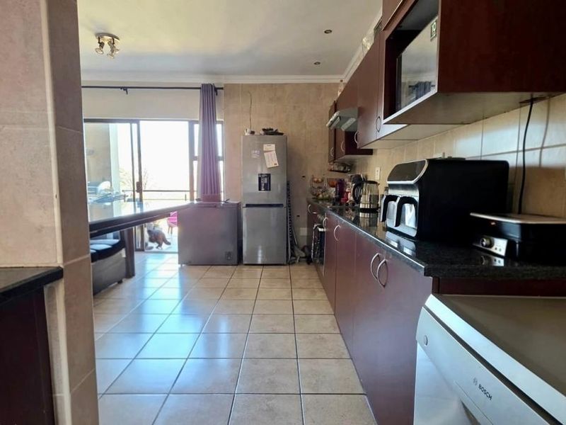 A functional kitchen featuring dark wood cabinetry, granite countertops, and tiled flooring, with an open-plan layout leading to a balcony.