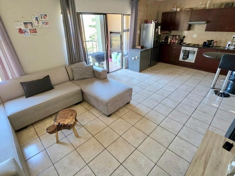 Open-plan living area featuring tiled floors, a functional kitchen with built-in cabinetry and appliances, and direct access to an outdoor balcony.