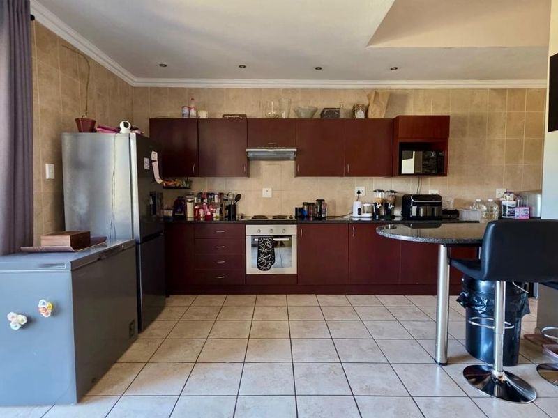 A functional kitchen featuring dark wood cabinetry, built-in oven and hob, tiled backsplash, and tiled flooring, offering a practical layout for daily use.