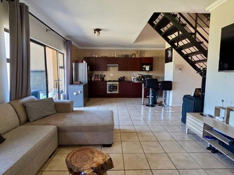 Open-plan living area featuring a kitchen with dark cabinetry, tiled flooring throughout, and a staircase leading to the upper level.