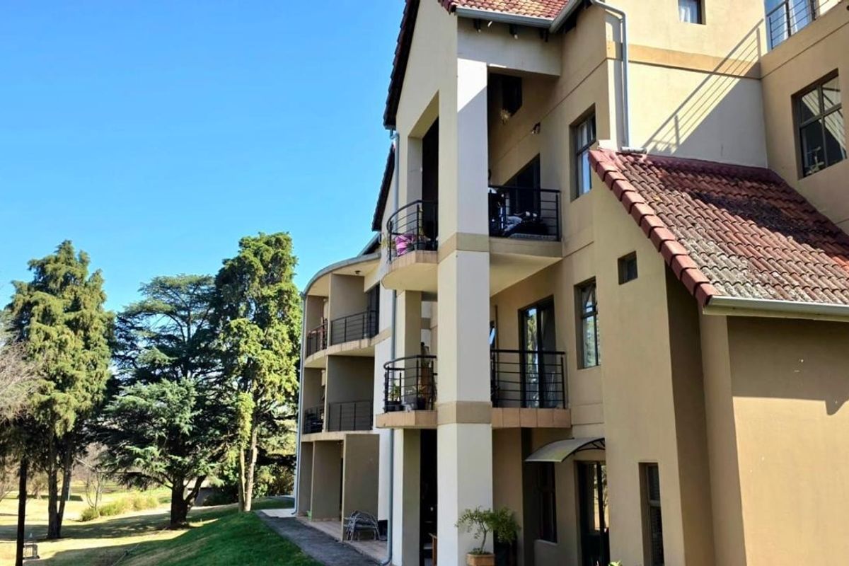 Rear elevation of a multi-story apartment building featuring stacked balconies with metal railings and a pitched tiled roof.