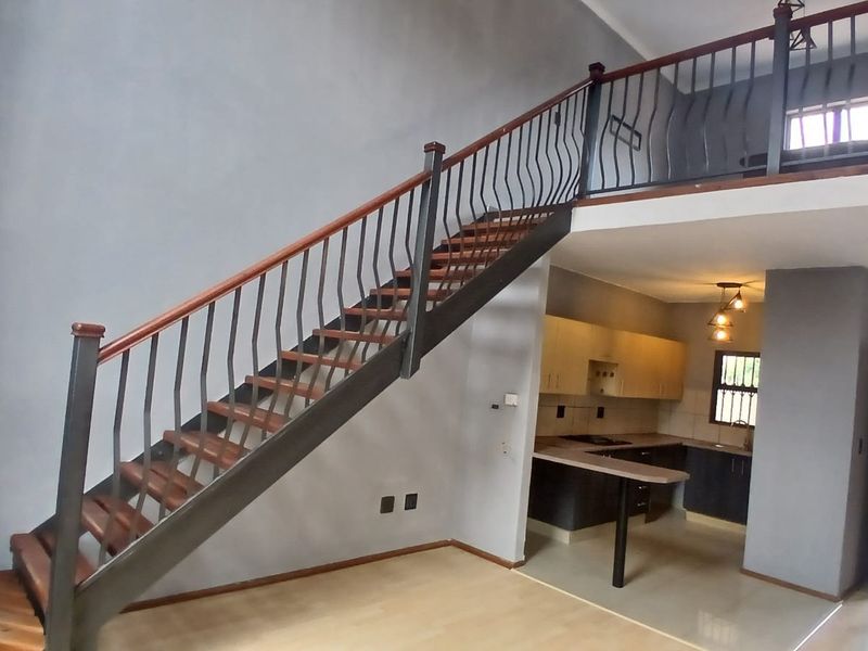Open-plan living area featuring a modern staircase with wooden treads, a mezzanine level, and a functional kitchen with built-in cabinetry and breakfast counter.